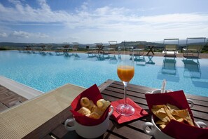 A poolside setting with lounge chairs, a glass of orange juice, and baskets of chips.