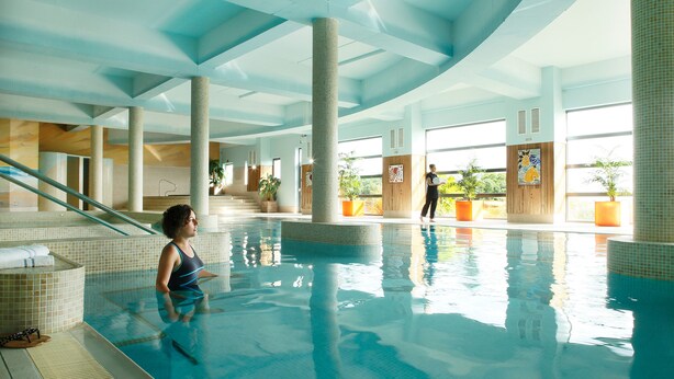 An indoor swimming pool with tiled walls and columns, a clear view of the pool, and a person standing by the pool. - Kinsale Hotel & Spa (Kinsale)