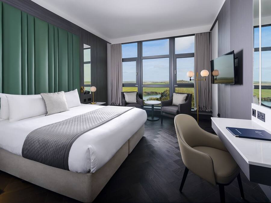 Habitación de hotel con una cama grande, un escritorio, una silla, un televisor y vistas al campo.