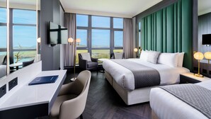 A modern hotel room with a large bed, a desk, and a chair. There is a TV mounted on the wall, and the room has large windows offering a view of the outdoors. - Kinsale Hotel & Spa (Kinsale)