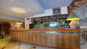 A bar area with a wooden counter, two lamps, and a wall of liquor bottles. - Ambassador Hotel (St. Paul's Bay)