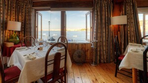 A dining area with tables set for two, a fan, and a view of the sea. - Ambassador Hotel (St. Paul's Bay)