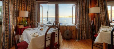 A dining area with tables set for two, a fan, and a view of the sea.