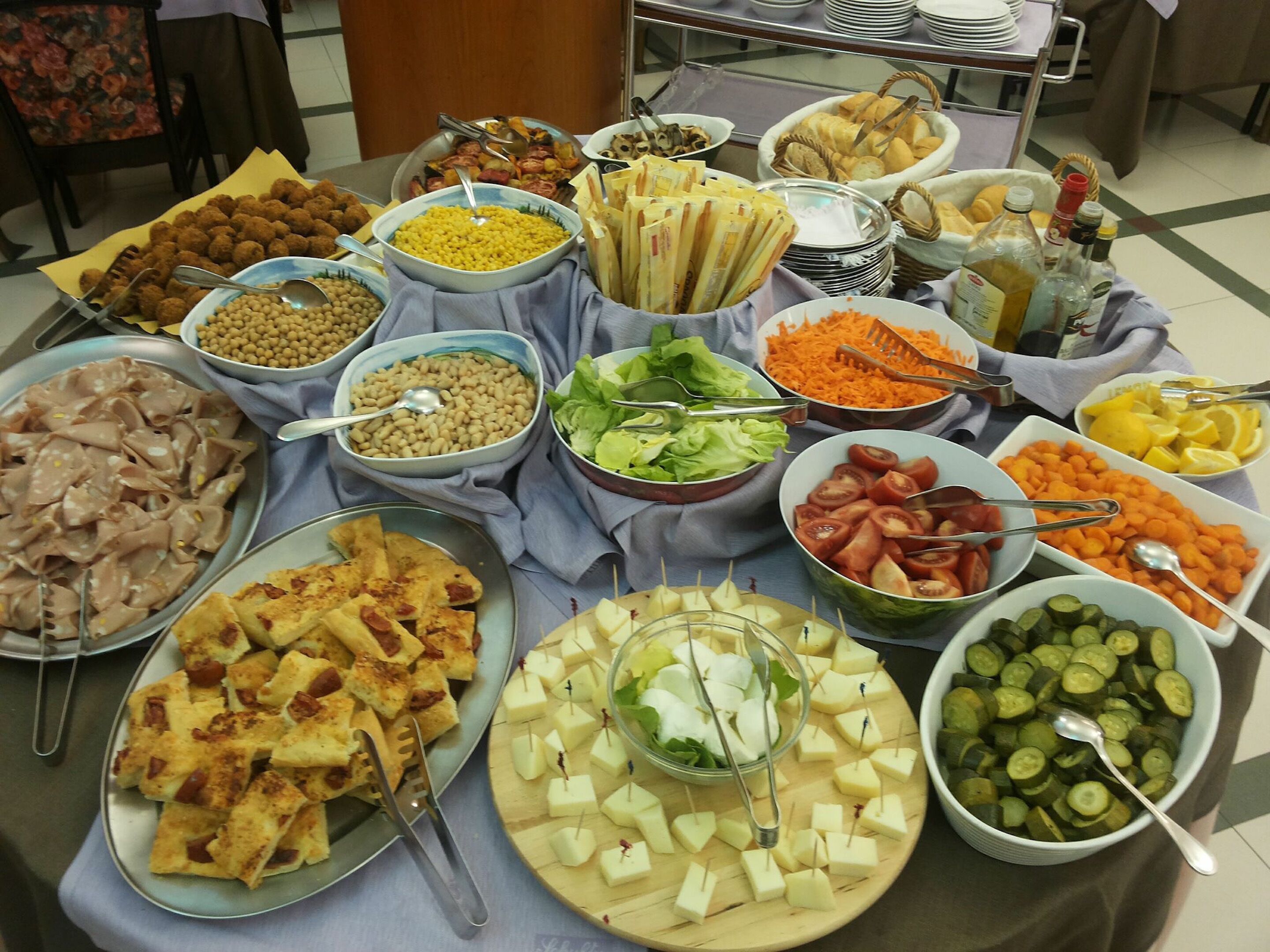 A buffet table with various food items including meats, cheeses, vegetables, and condiments.