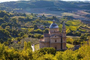 Una iglesia histórica con una imponente torre campanario, rodeada de abundante vegetación y colinas ondulantes.