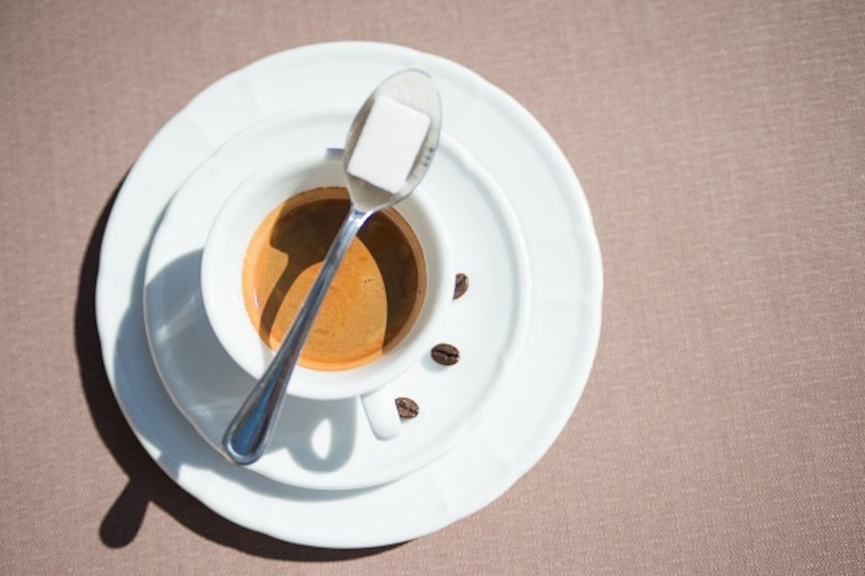 Una tazza di caffè bianco con un cucchiaino e un cubetto di zucchero su un piattino.