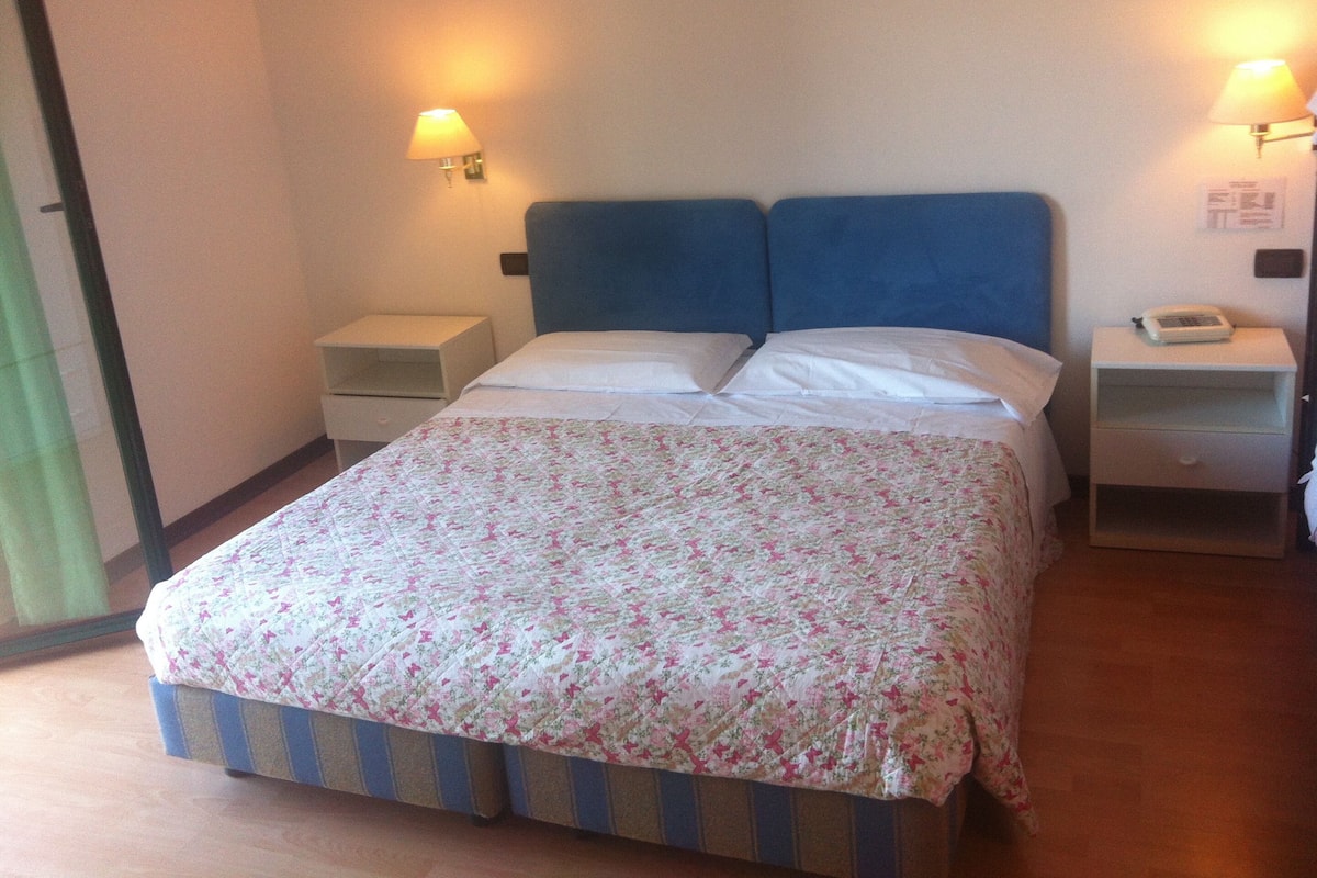 A standard hotel room with a double bed, two bedside tables, and two wall-mounted lamps.