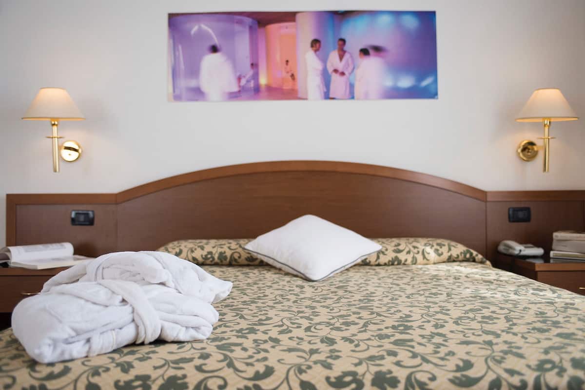 A hotel room with a neatly made bed, two bedside lamps, a wall-mounted artwork, and a wooden headboard.