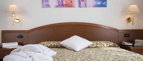 A hotel room with a neatly made bed, two bedside lamps, a wall-mounted artwork, and a wooden headboard.