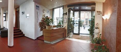 A hotel lobby with a reception desk, a staircase, and a glass door leading outside.