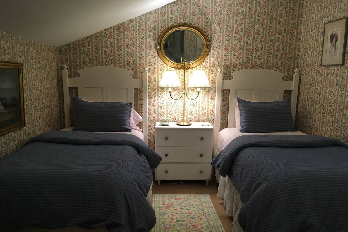 Une chambre avec deux lits simples, une table de chevet avec une lampe, un miroir et un papier peint à motifs floraux.