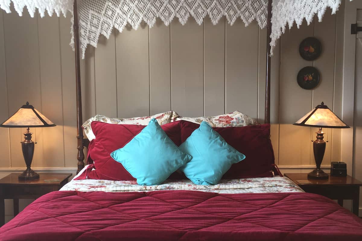 Un lit avec une couette rouge, deux oreillers et un baldaquin en dentelle. Il y a deux tables de chevet avec des lampes.