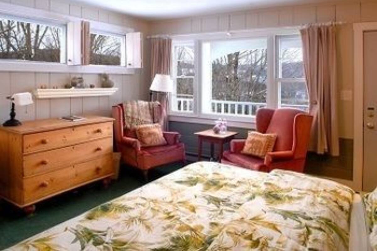 Une chambre à coucher comprenant un lit, une commode, deux chaises, une petite table et une fenêtre avec des rideaux.