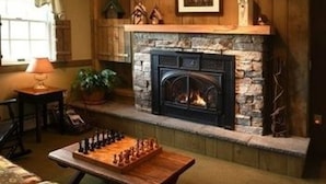 Una habitación acogedora con chimenea de piedra, un tablero de ajedrez en una mesa y una ventana con cortinas.