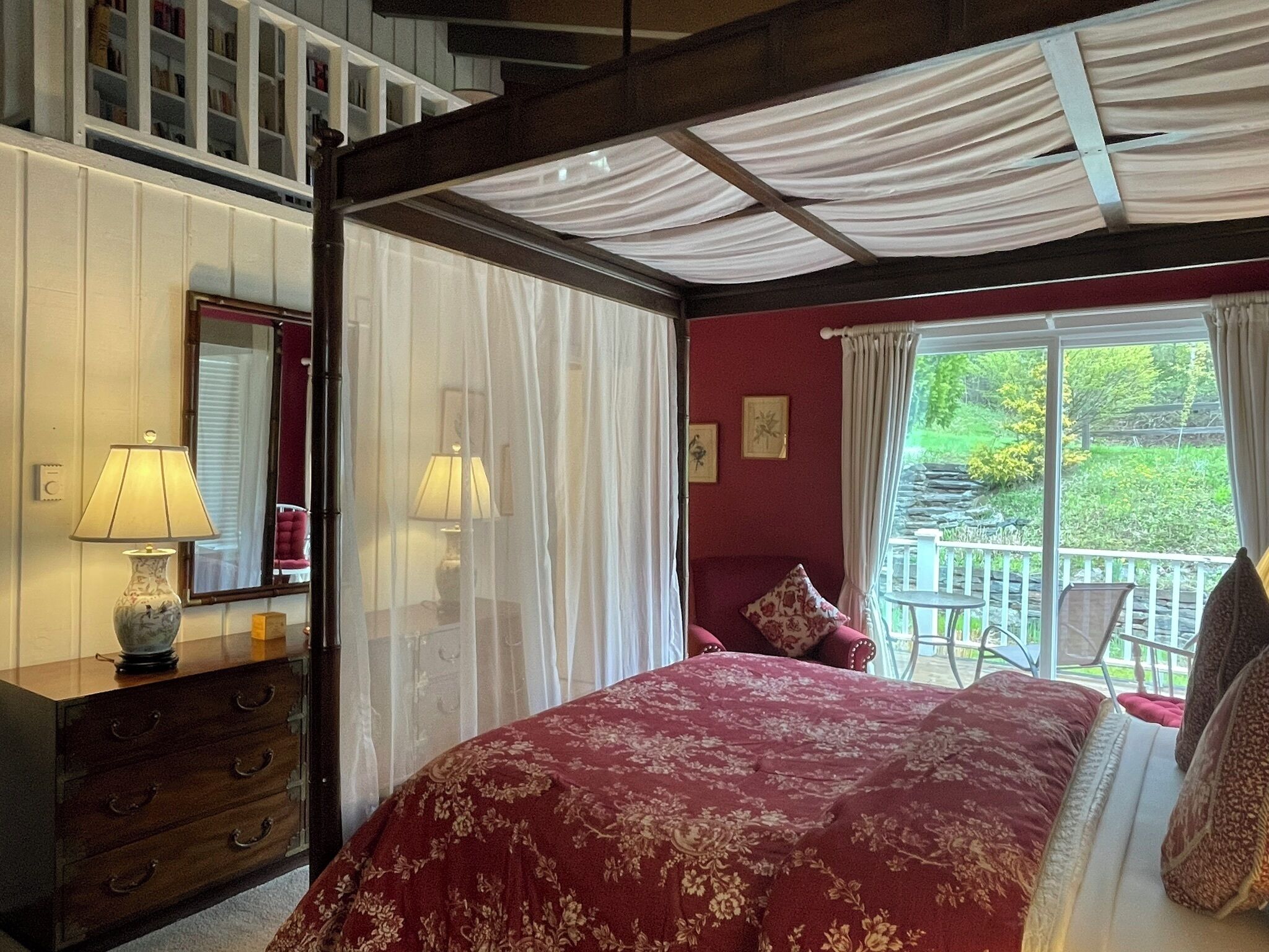 A bedroom with a large bed, a wooden dresser, a mirror, and a window with curtains.