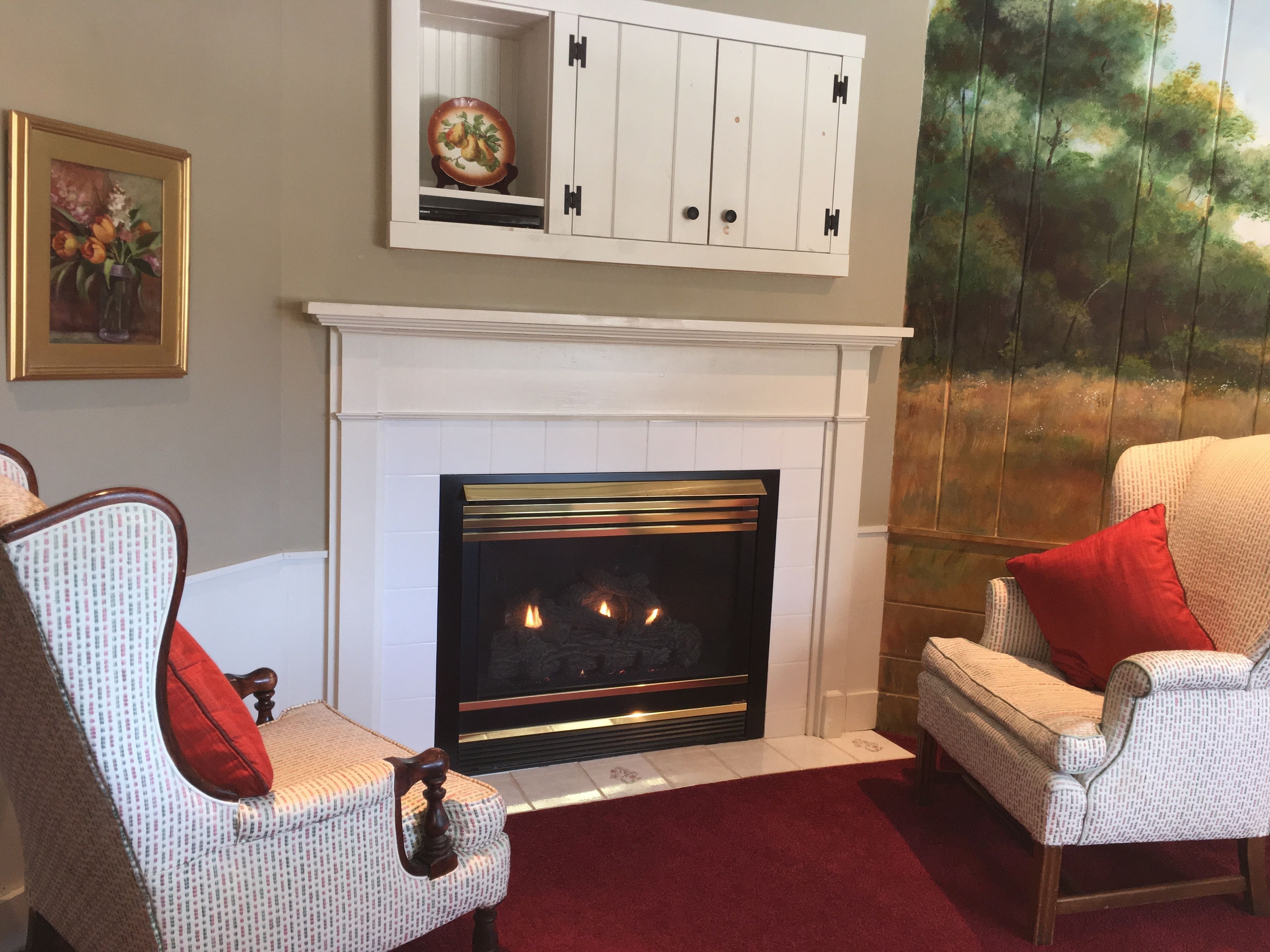 A living room with a fireplace, patterned chairs, a red rug, and a painting on the wall.