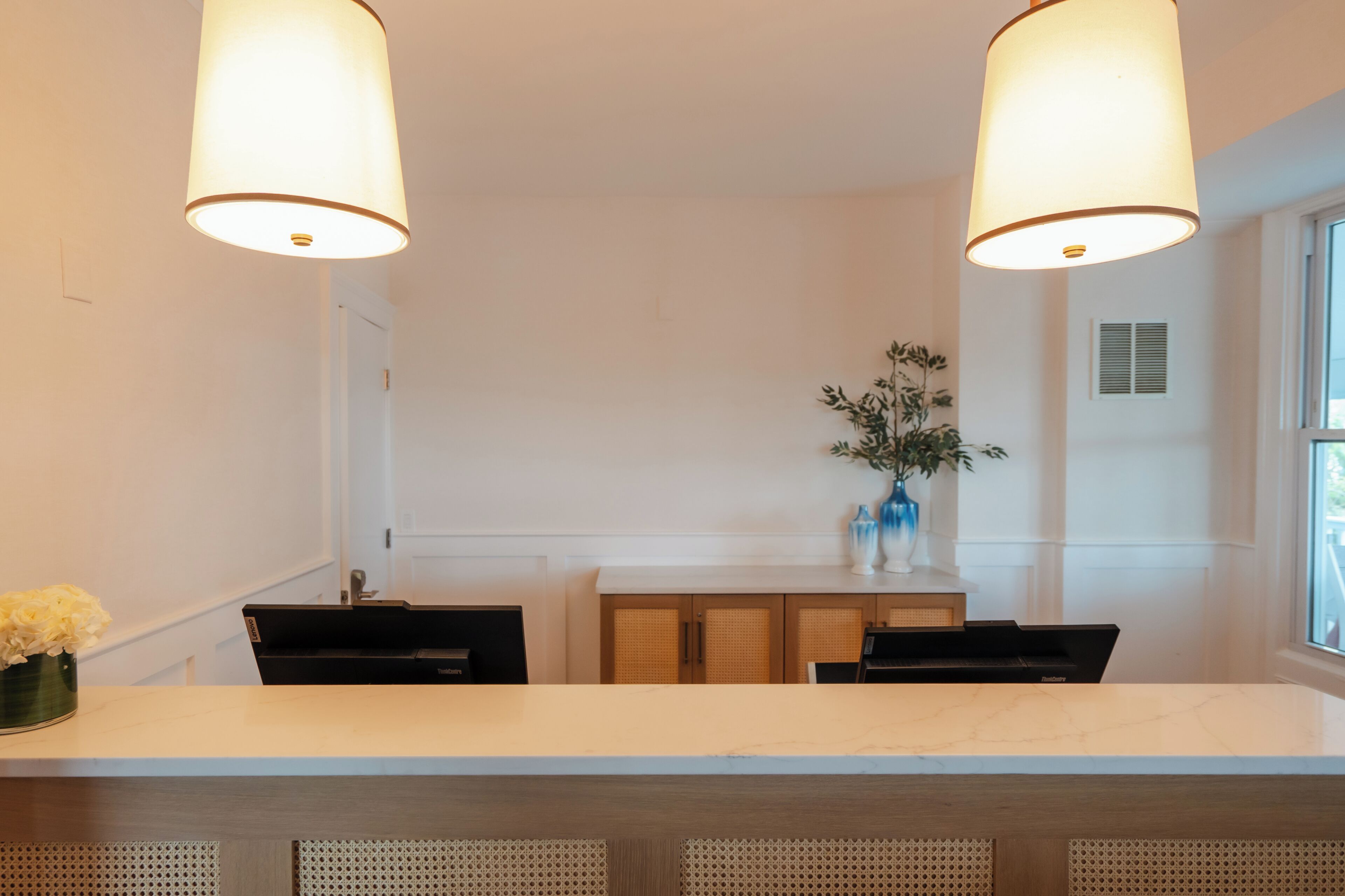 Een moderne keuken met een marmeren aanrecht, twee hanglampen, een houten kast en een bloemenvaas.