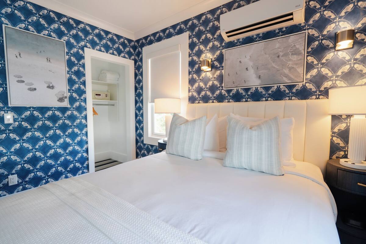 Ein Hotelzimmer mit einem Bett, einem Nachttisch, einer Wand-Klimaanlage und einer Tür zu einem Badezimmer.
