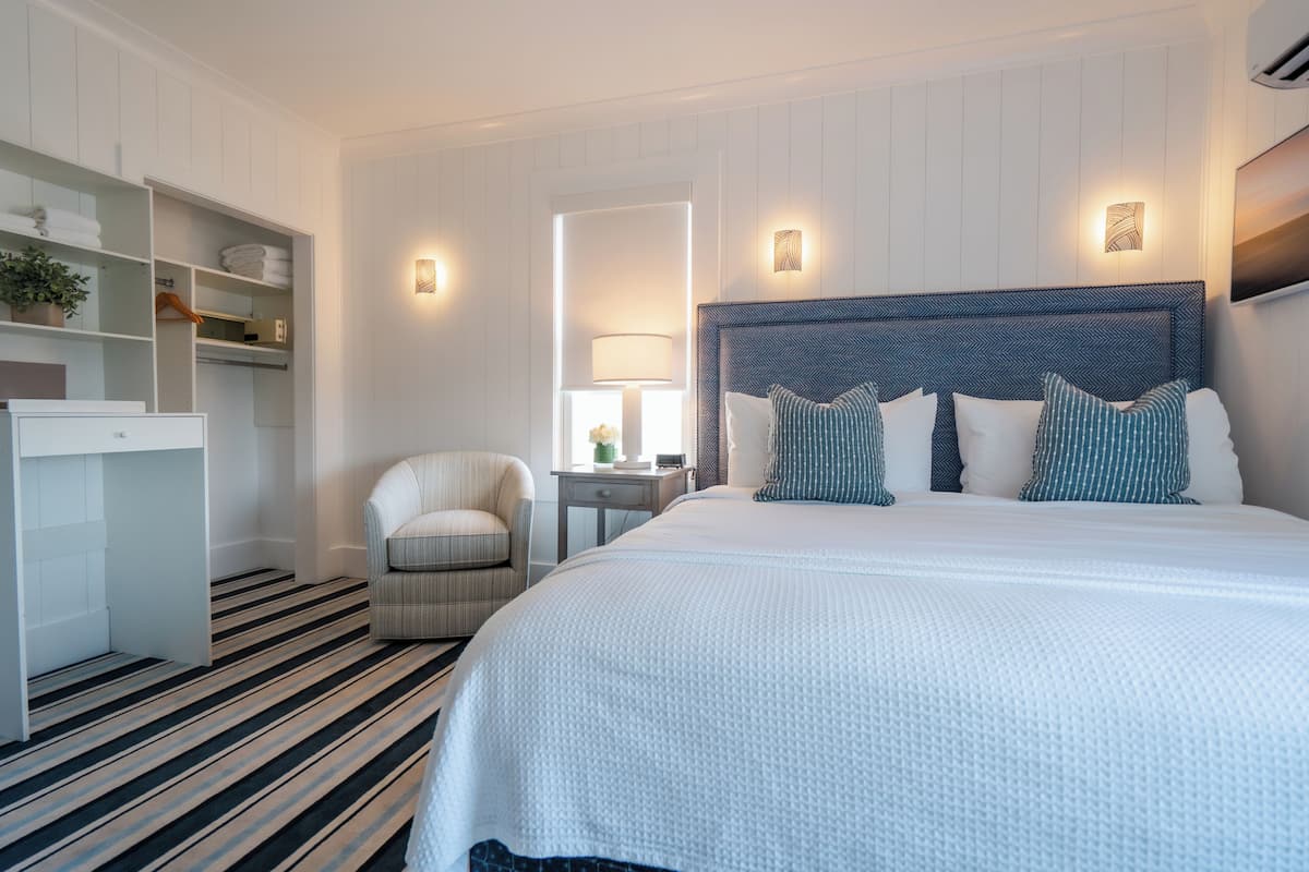 Ein Hotelzimmer mit einem großen Bett, einem Sessel, einem Schreibtisch und einem Kleiderschrank.