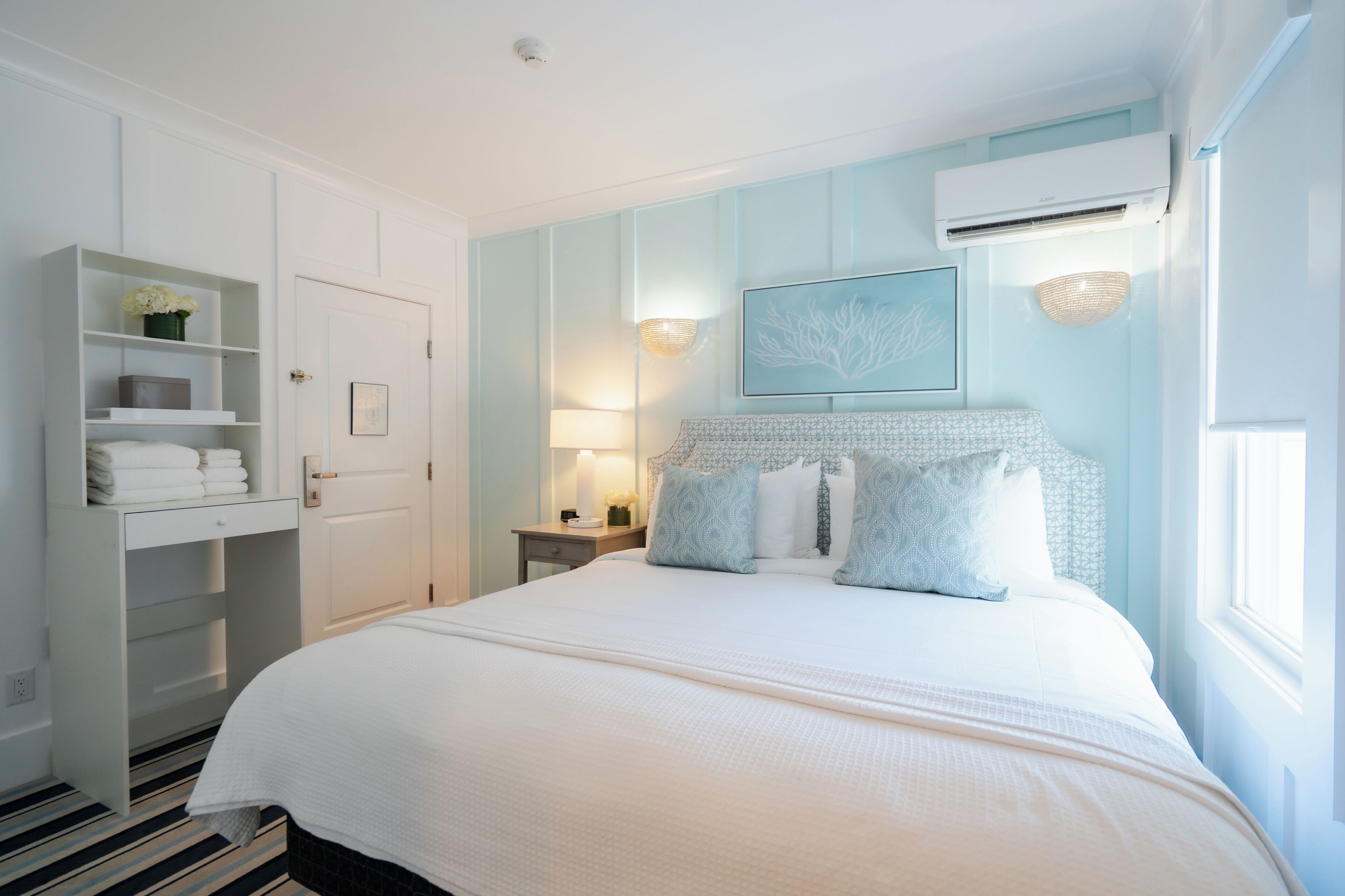 A neatly arranged bedroom with a bed, a wardrobe, a nightstand, and a wall-mounted air conditioner.