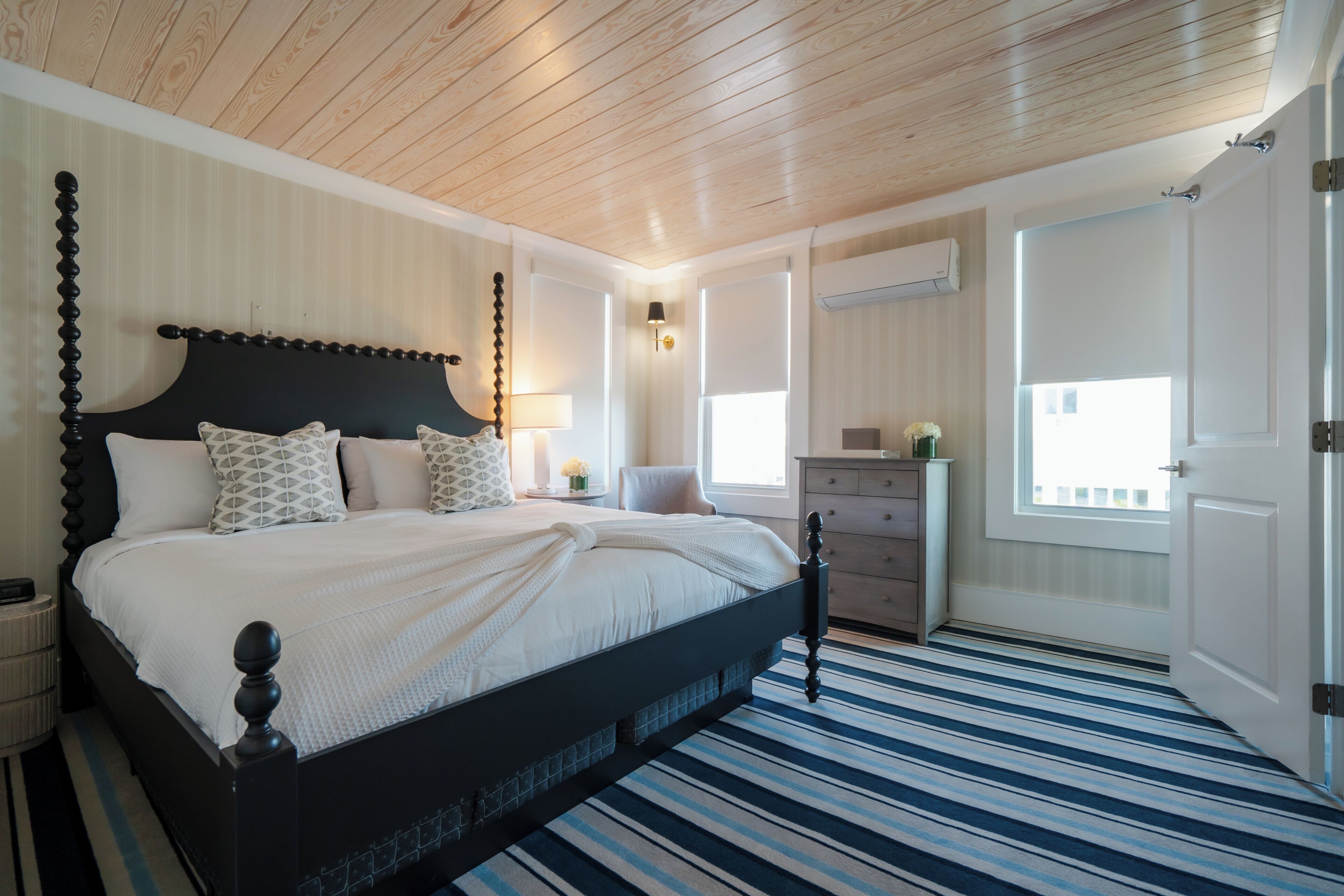 Un dormitorio con cama, mesitas de noche, cómoda, ventana y puerta.