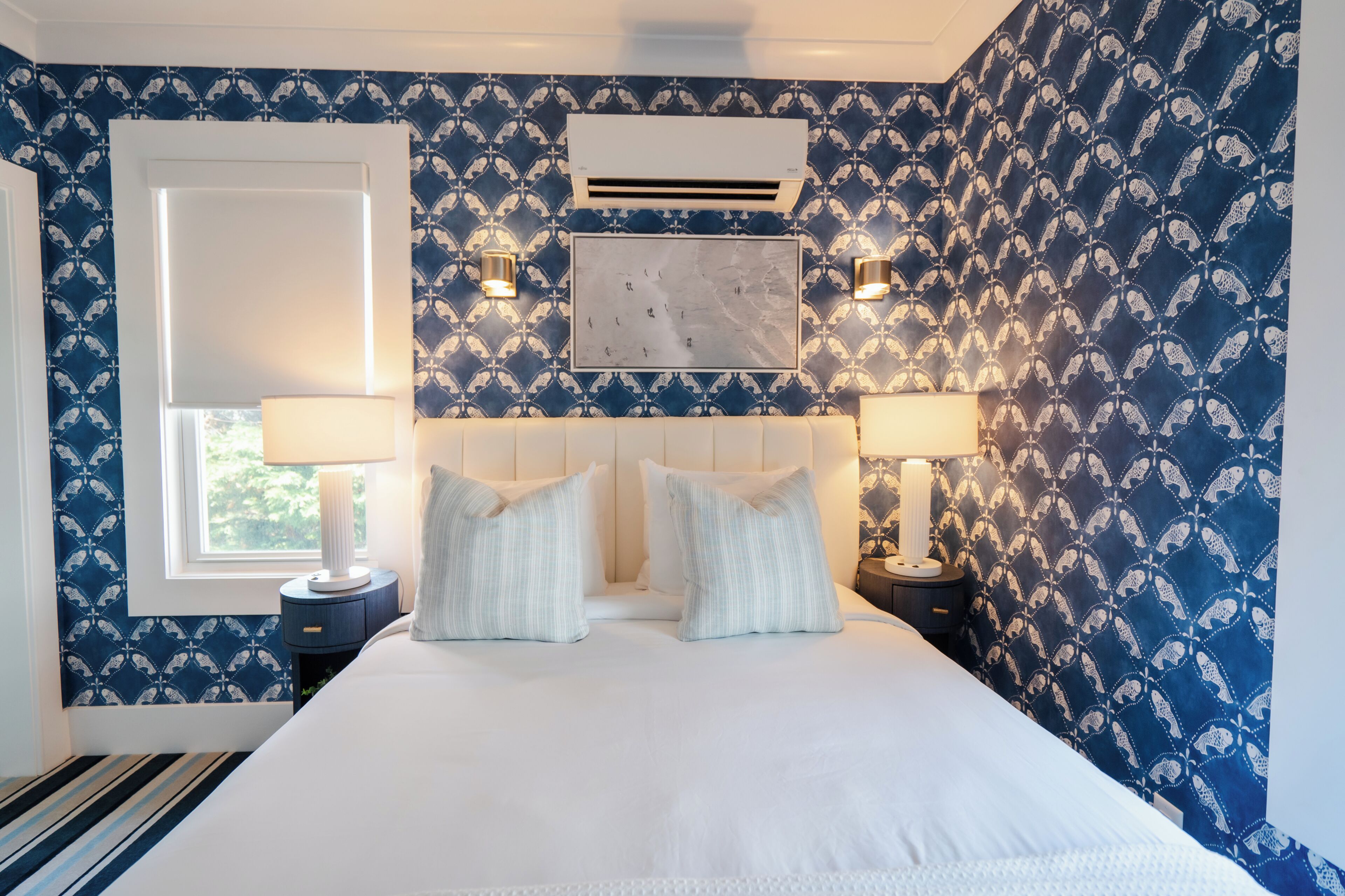 A bedroom with a large bed, two bedside lamps, an air conditioner, and patterned wallpaper.