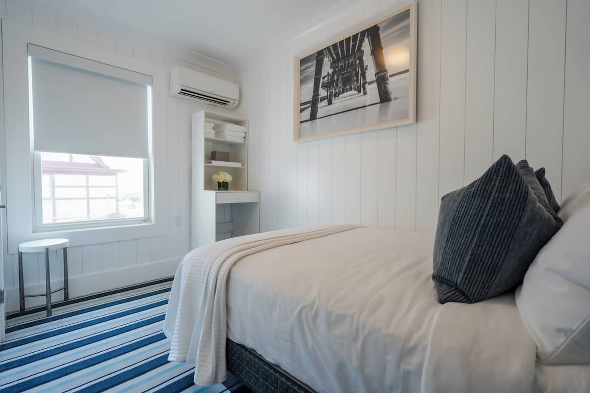 Ein Schlafzimmer mit Bett, Fenster, einer weißen Klimaanlage und einem gerahmten Bild an der Wand.