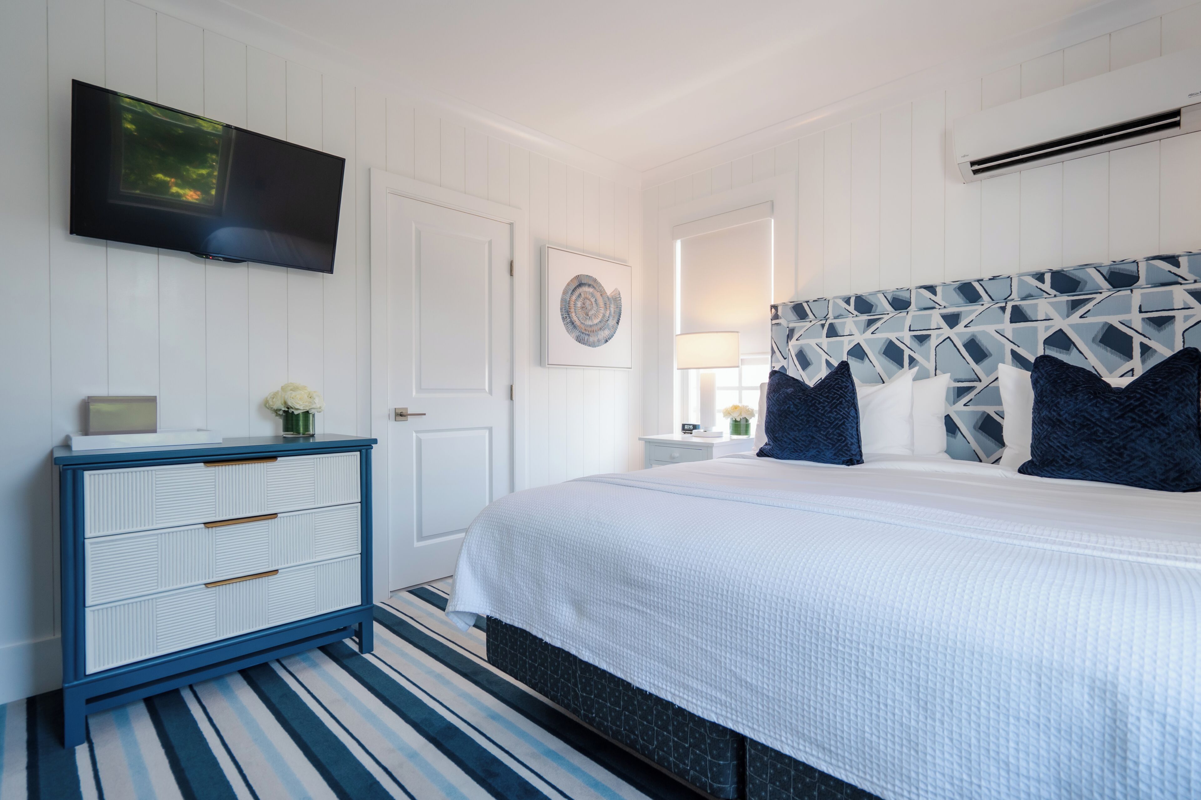 A bedroom with a bed, a dresser, a TV, and a wall-mounted artwork.