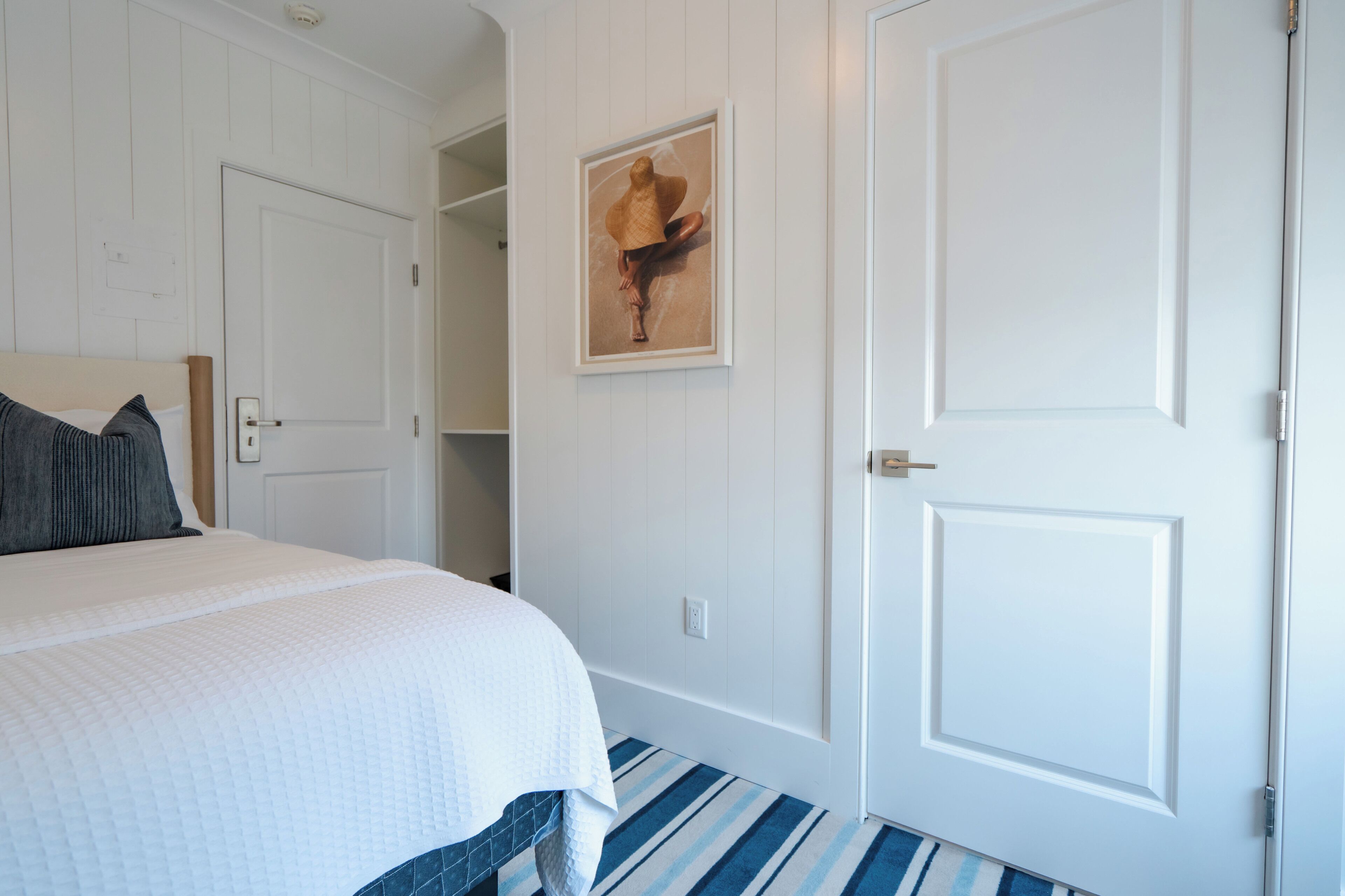 A bedroom with a bed, a door, and a framed picture on the wall.