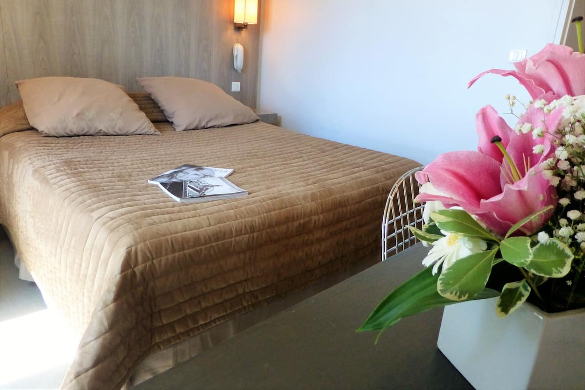 Ein Hotelzimmer mit einem Bett, einem Nachttisch, einer Lampe und einer Blumenkomposition.