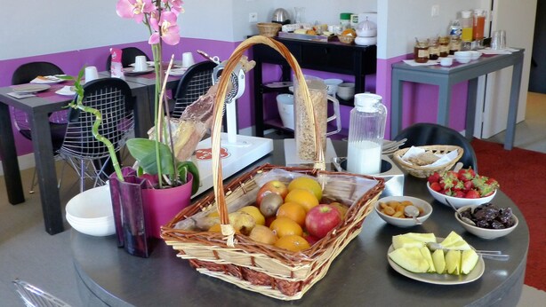 A breakfast buffet setup with various fruits, a wicker basket, and a vase of pink orchids. - Bliss Hôtel (Cogolin)