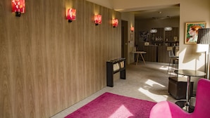A modern lobby with wooden paneling, a pink rug, a black bookshelf, and a reception desk. - Bliss Hôtel (Cogolin)