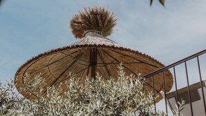 A thatched umbrella structure with a decorative top, surrounded by olive trees.