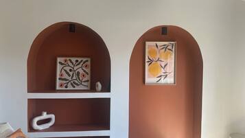 A bedroom with a bed, two wall-mounted shelves with artwork, and a bedside table with a lamp.