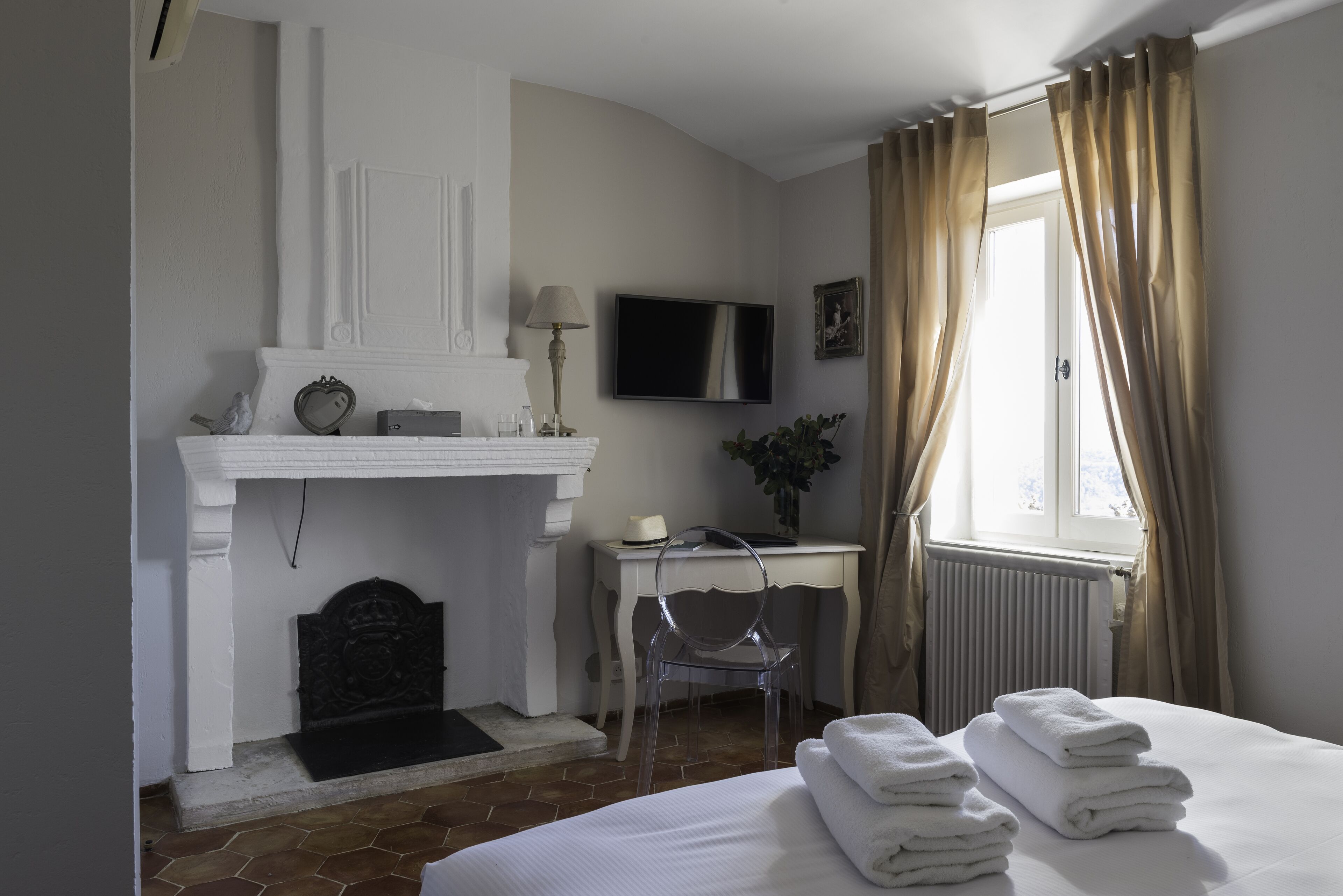 Habitación de hotel con chimenea, un escritorio, una silla, una cama con toallas, un televisor y cortinas.