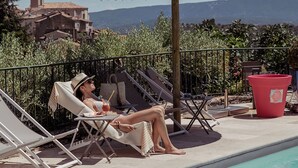 A poolside area with lounge chairs, a thatched umbrella, and a view of the landscape.