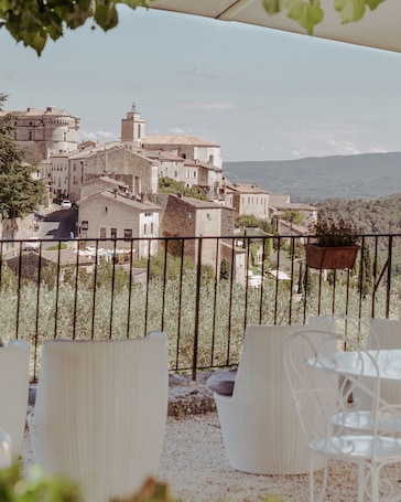 A terrace with wicker chairs and a view of a historic town with stone buildings and a mountain in the background.