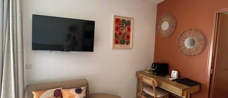 Una sala de estar con un sofá, un televisor, un escritorio y detalles decorativos en la pared.