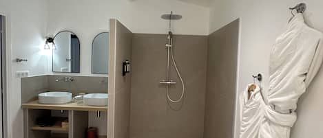 A modern bathroom with a shower, two sinks, and a robe hanging on the wall.