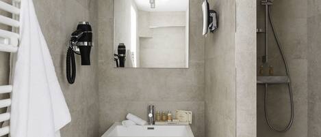 A modern bathroom with a white sink, a mirror, a hairdryer, and a shower.