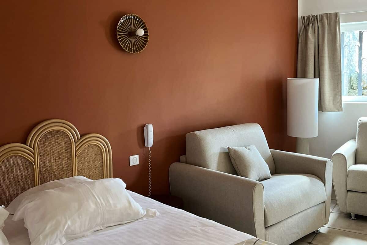 A hotel room with a bed, a sofa, a lamp, and a wall clock.