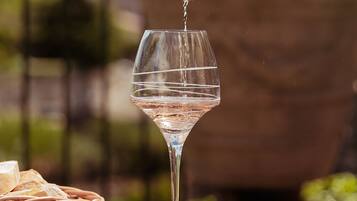 Una mano vertiendo un líquido transparente en una copa de vino, con una cesta de mimbre y alimentos en primer plano.