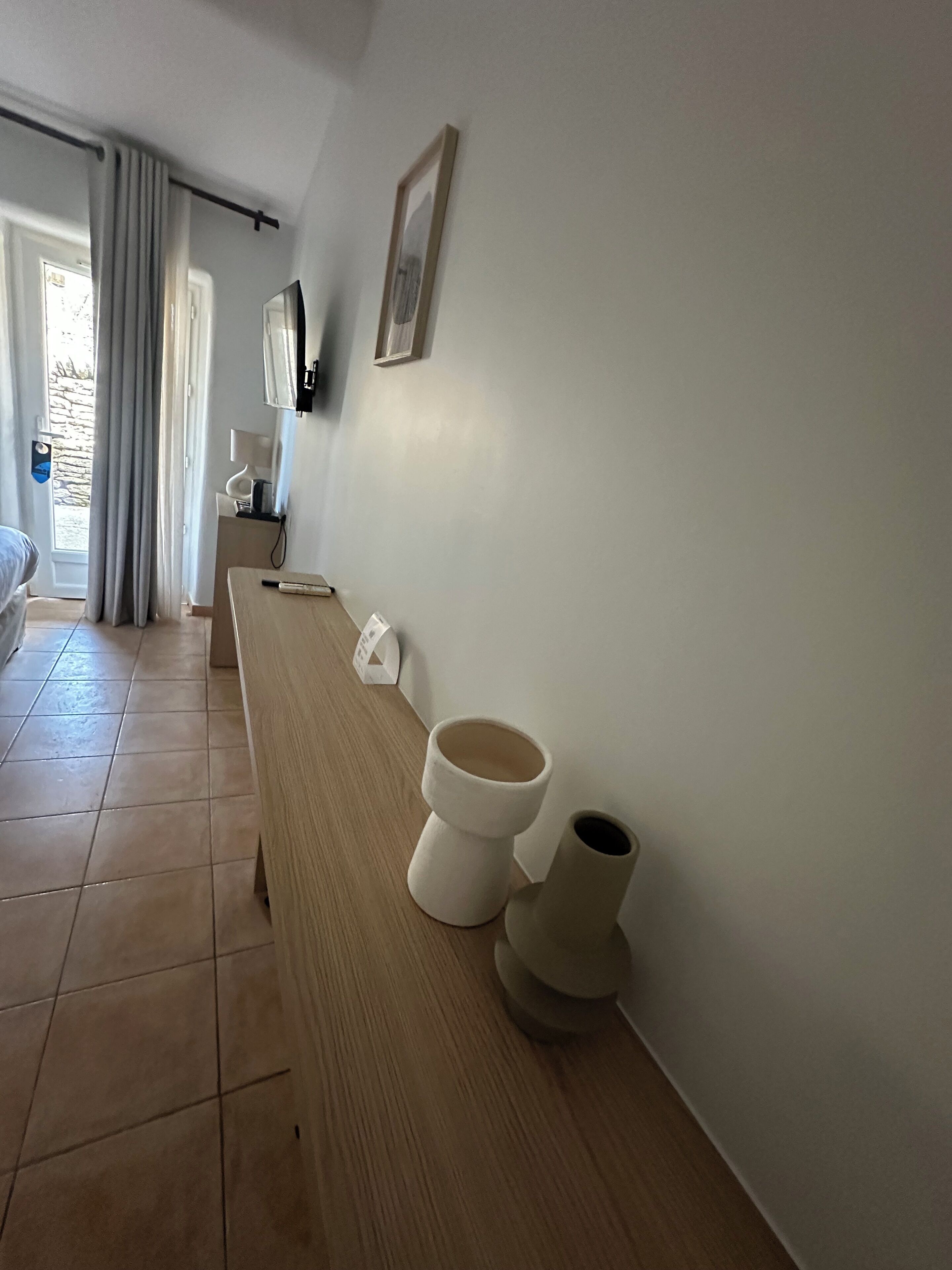 A hotel room with a wooden bench, two toilets, a framed picture on the wall, and a window with curtains.