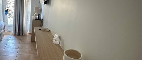 Habitación de hotel con un banco de madera, dos inodoros, un cuadro enmarcado en la pared y una ventana con cortinas.