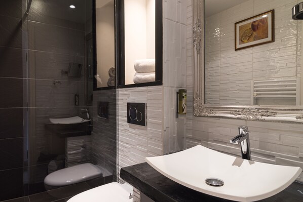 Un baño moderno con ducha envuelta en vidrio, un lavamanos blanco sobre encimera negra y un espejo grande.