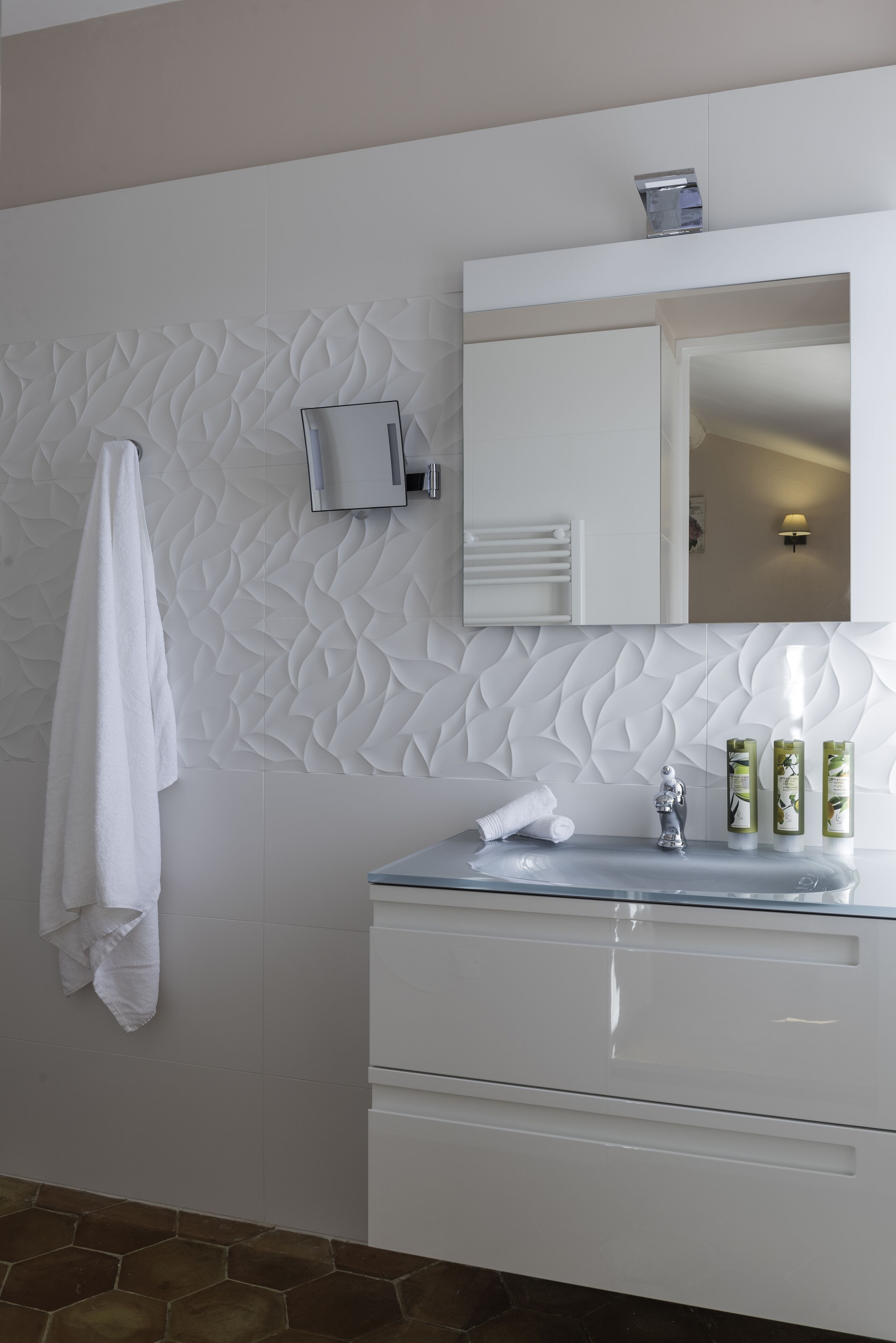 A modern bathroom with a white vanity, a large mirror, and a textured wall.