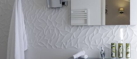 A modern bathroom with a white vanity, a large mirror, and a textured wall.