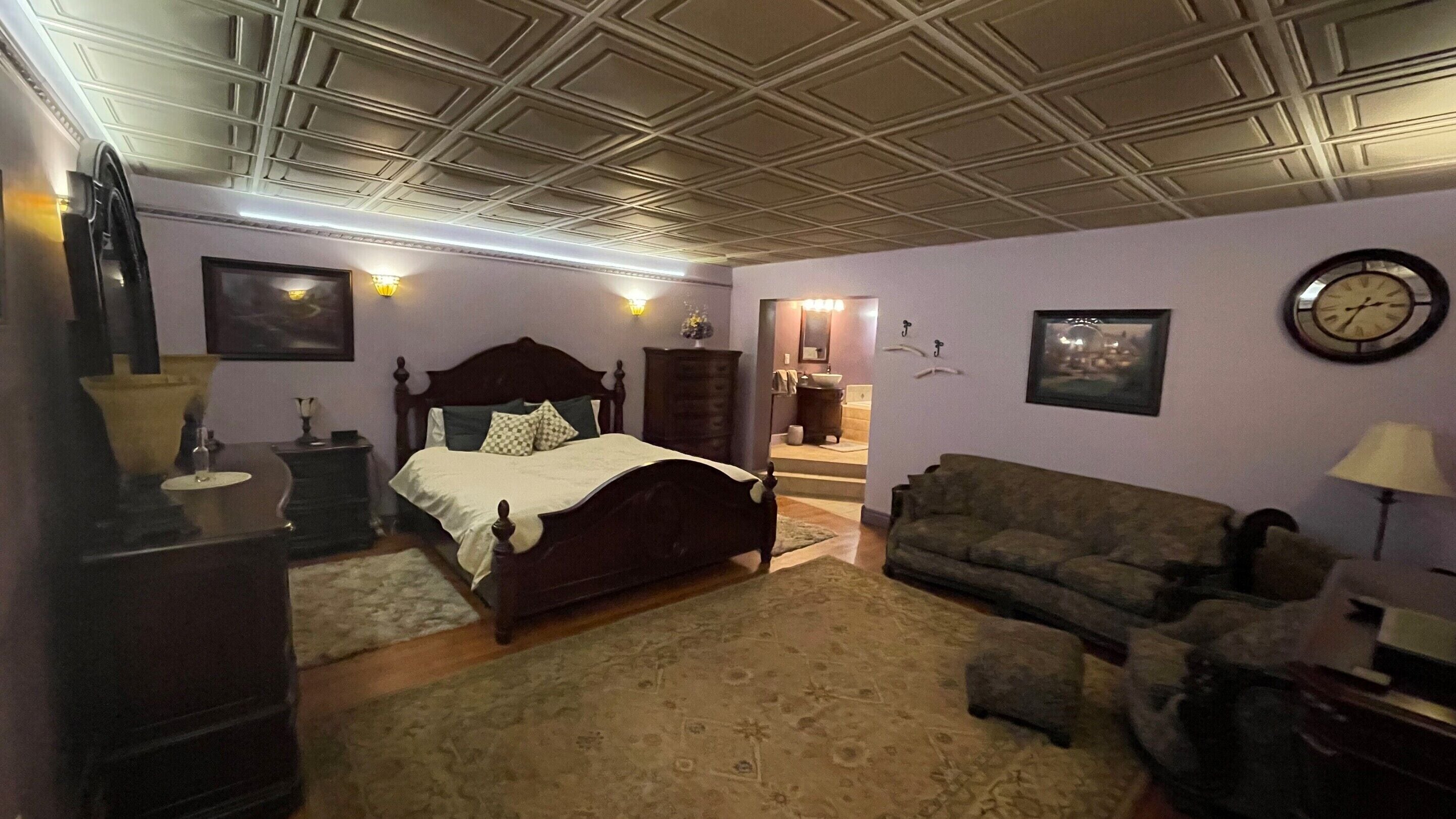 Un dormitorio con cama, sofá, cómoda, espejo y un reloj en la pared.