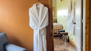 A room with a wooden floor, a blue sofa, and a white robe hanging on a wooden hanger. - The Yorkshire Inn (Phelps)