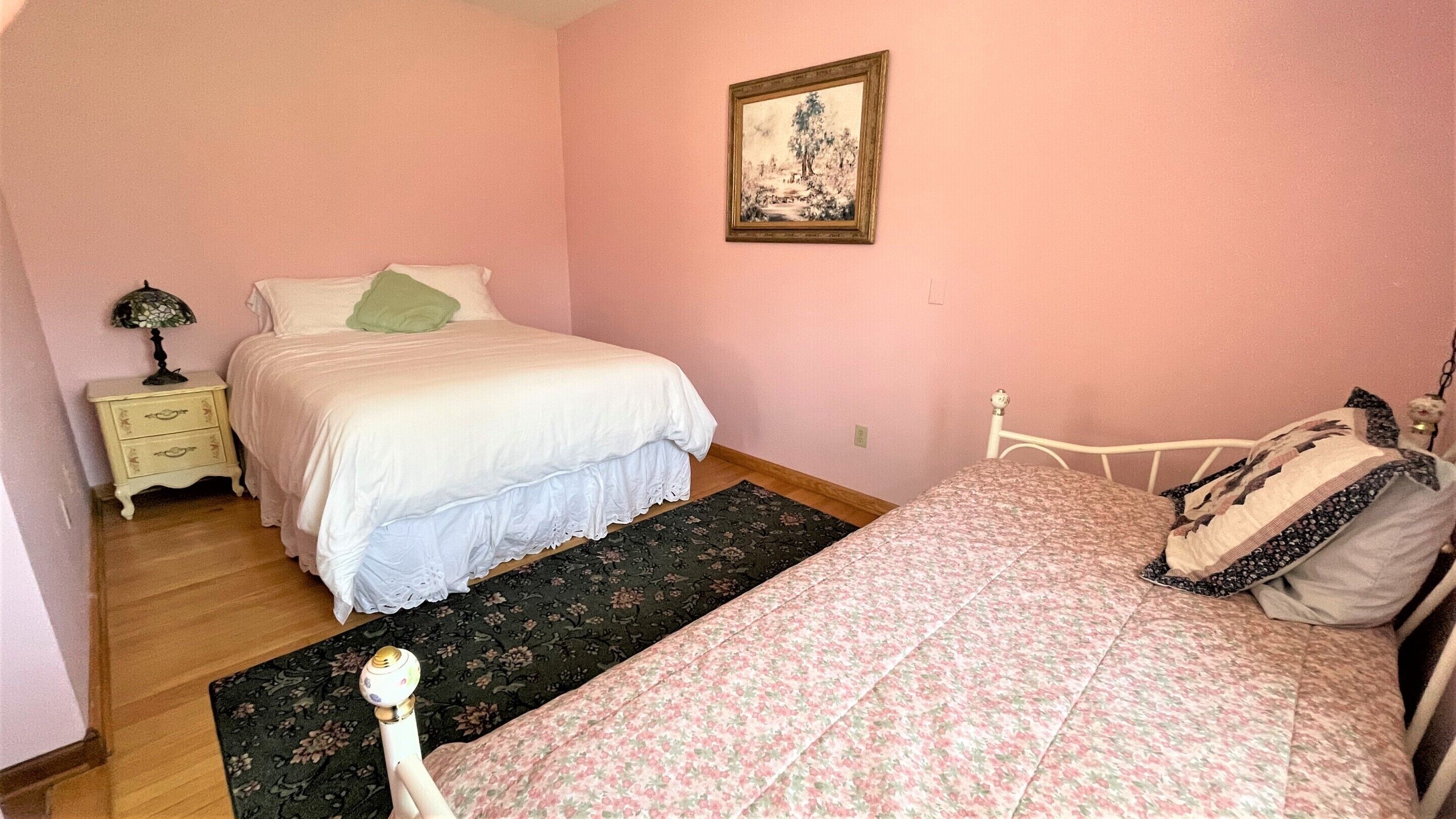 A bedroom with two beds, a nightstand, a lamp, and a framed picture on the wall.